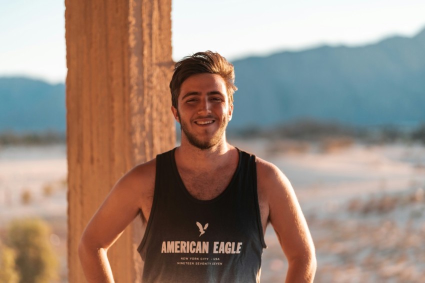 man in black tank top standing beside brown wooden wall during daytime
