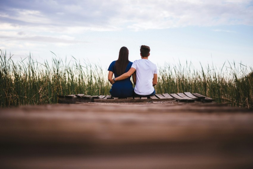 man and woman sitting on brown wooden pathway surrounded by green grass during daytime