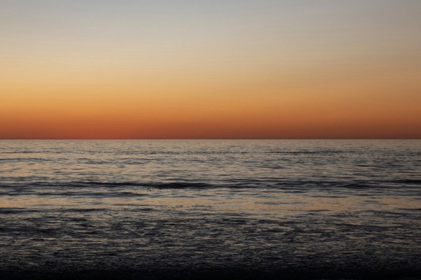 the sun is setting over the ocean on a beach