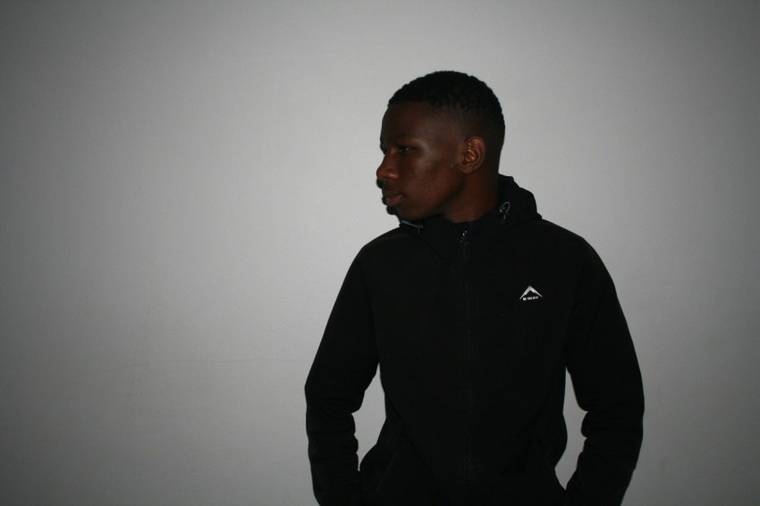 a man in a black hoodie standing in front of a white wall