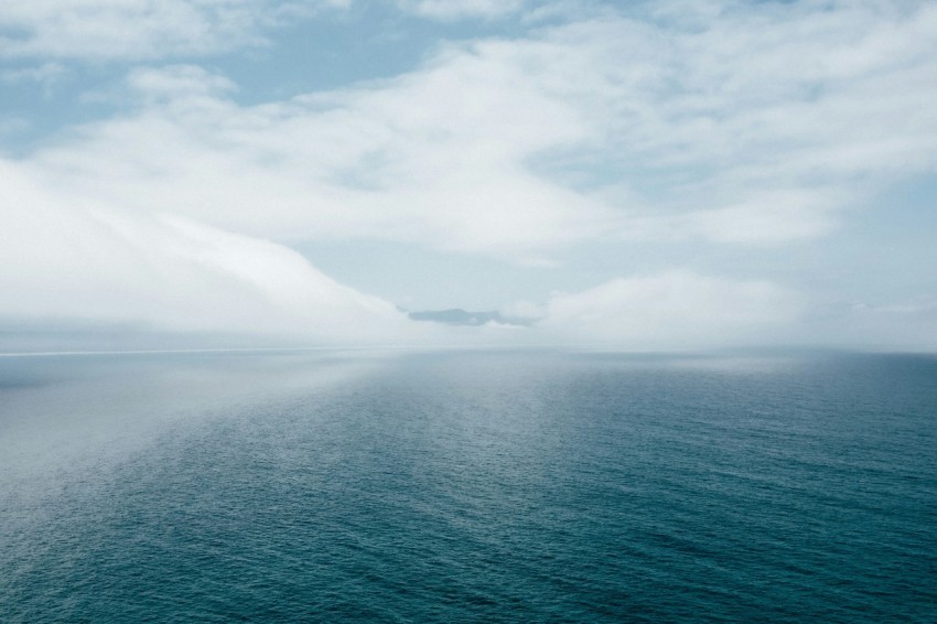 body of water near mountain under white clouds during daytime