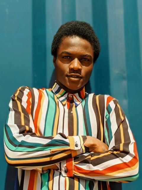a man with his arms crossed standing in front of a blue wall