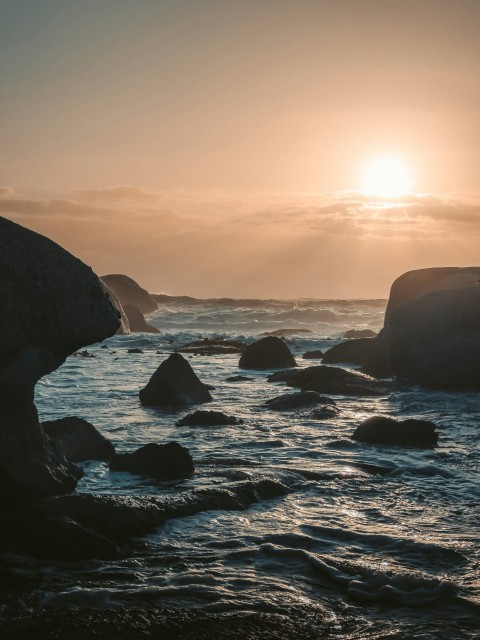 the sun is setting over the ocean with rocks in the foreground Hb5vcgm