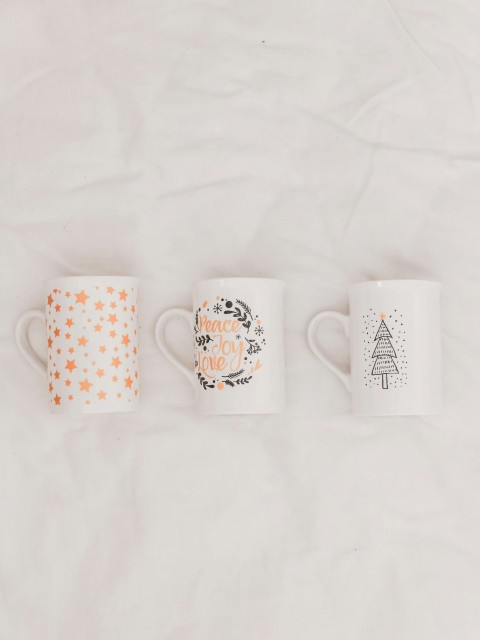 three white and multicolored ceramic mugs on white textile Wasu92