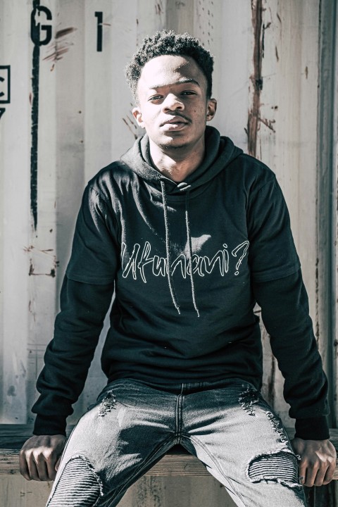 man in black nike hoodie and blue denim jeans sitting on white wooden bench